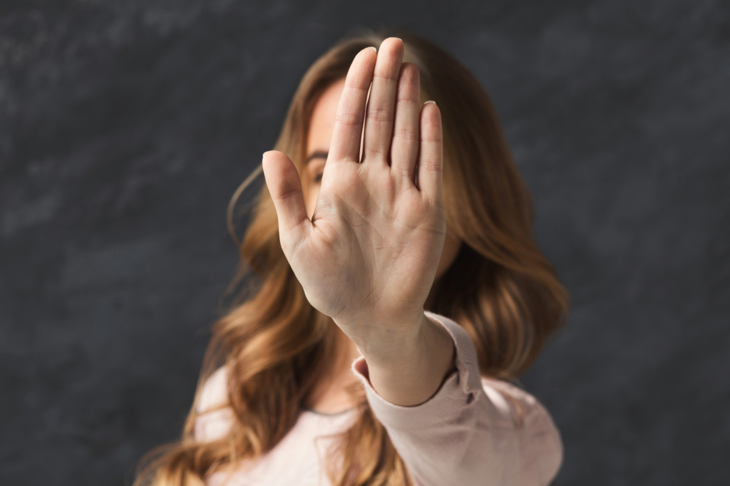 Femme levant une main devant elle pour faire signe d'arrêter, illustrant une situation de protestation ou de résistance face à une forme de discrimination