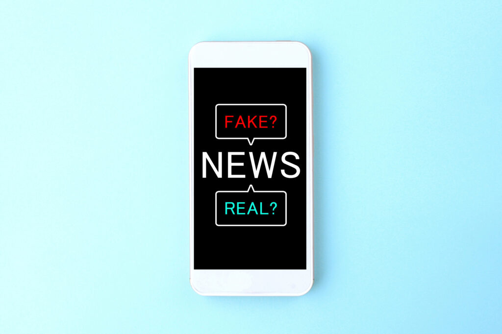 Téléphone posé sur un fond bleu affichant un message avec "news?" suivi de deux réponses possibles : "fake?" et "real?", illustrant une situation liée à la diffusion d'informations douteuses ou à la diffamation