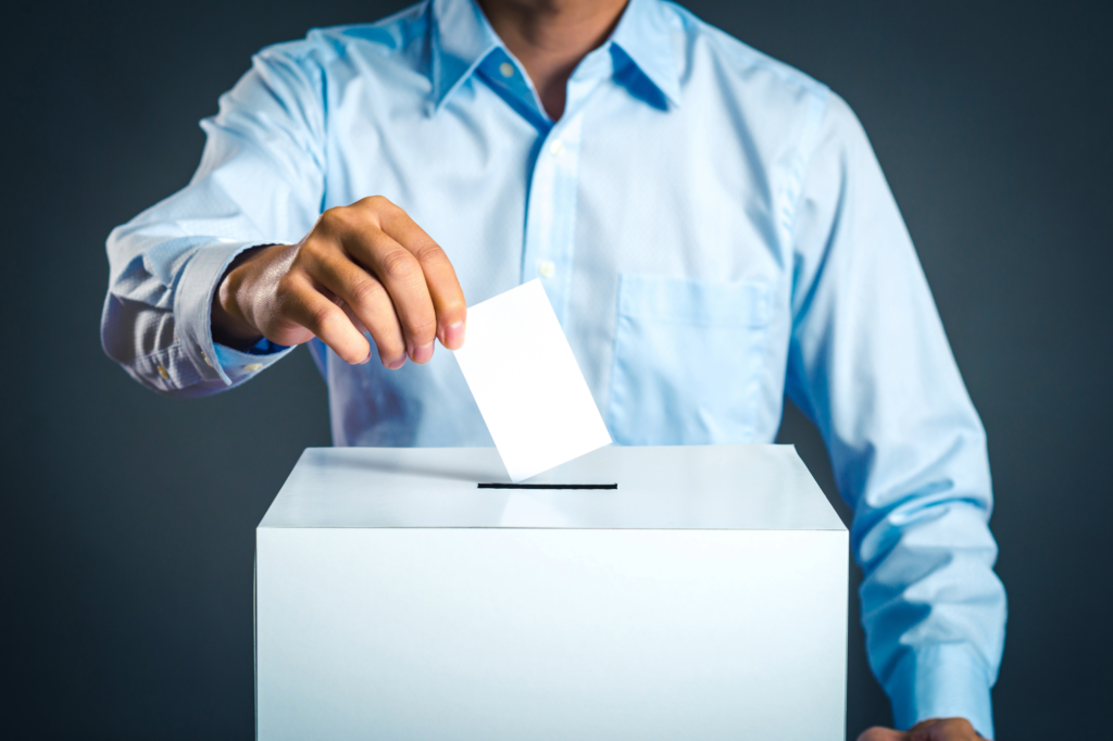 Homme en chemise glissant son bulletin de vote dans une urne