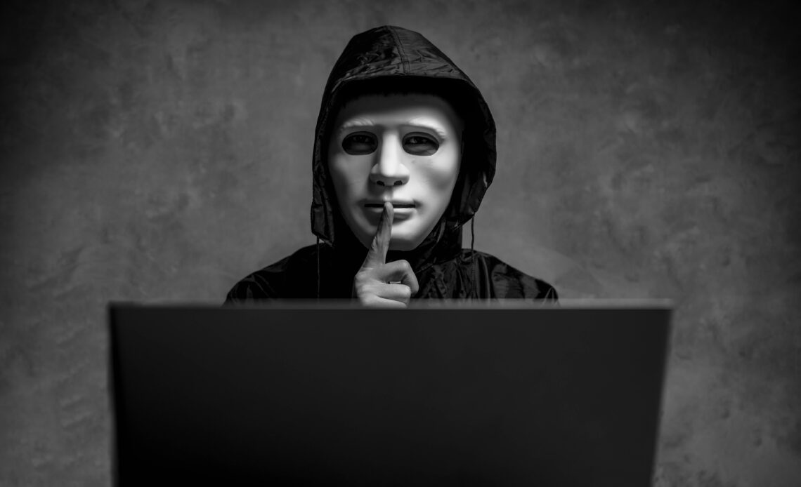 Homme caché derrière un masque et devant un ordinateur