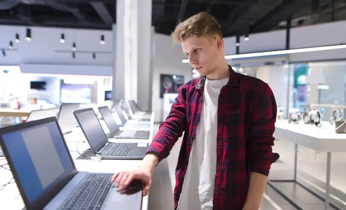 Un jeune homme dans un magasin d'ordinateurs en train de choisir son pc portable