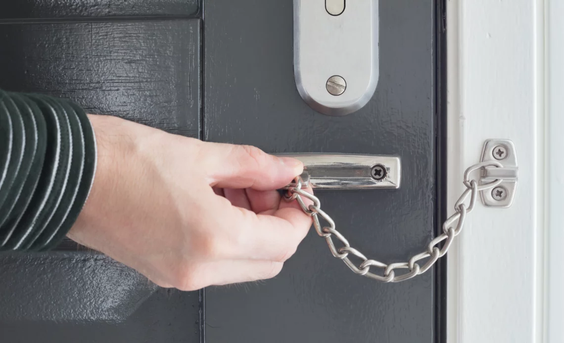 Homme utilisant un entrebâilleur à chaine sur une porte blindée