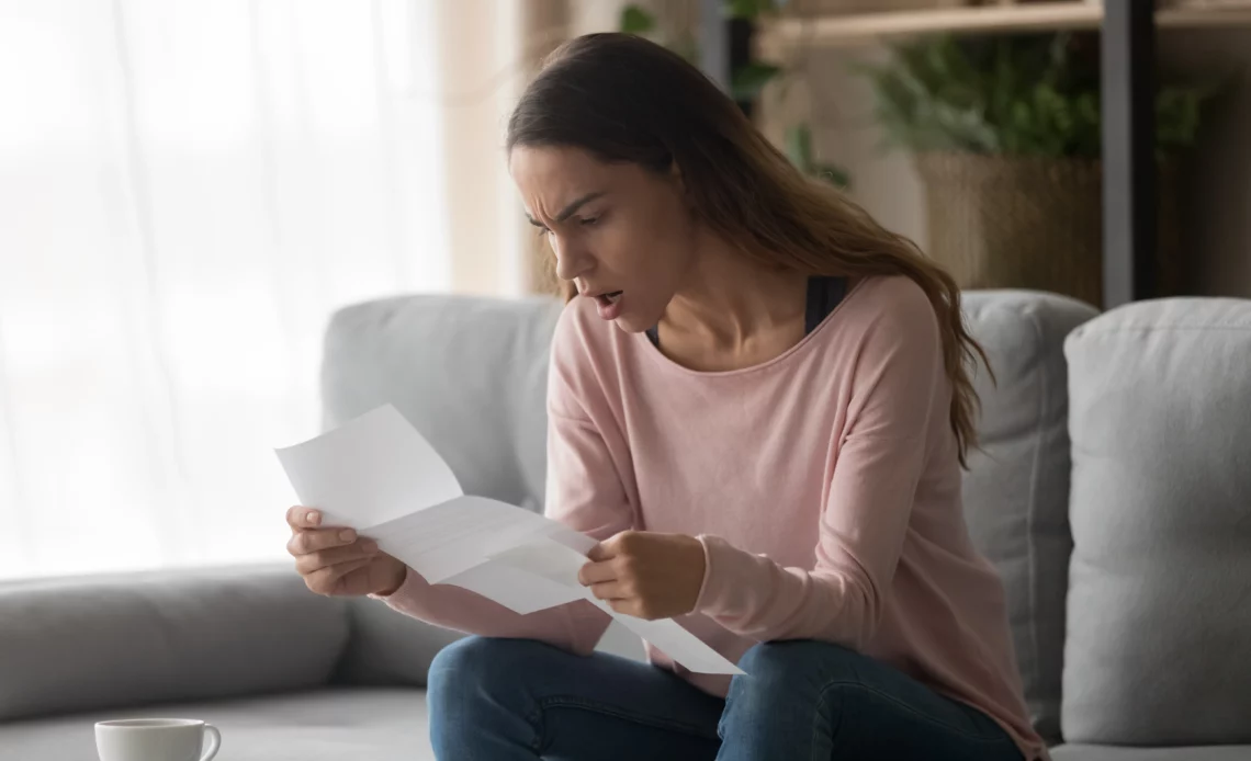 Femme assise sur un canapé lisant un papier pour illustrer une amende pour tapage nocturne sans avertissement