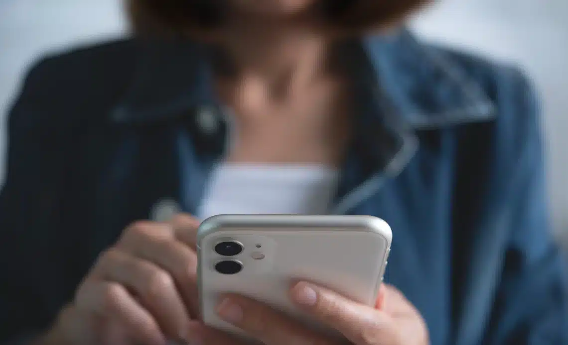 Femme avec un téléphone portable entre les mains pour illustrer une personne qui se demander qui appeler en cas de tapage nocturne