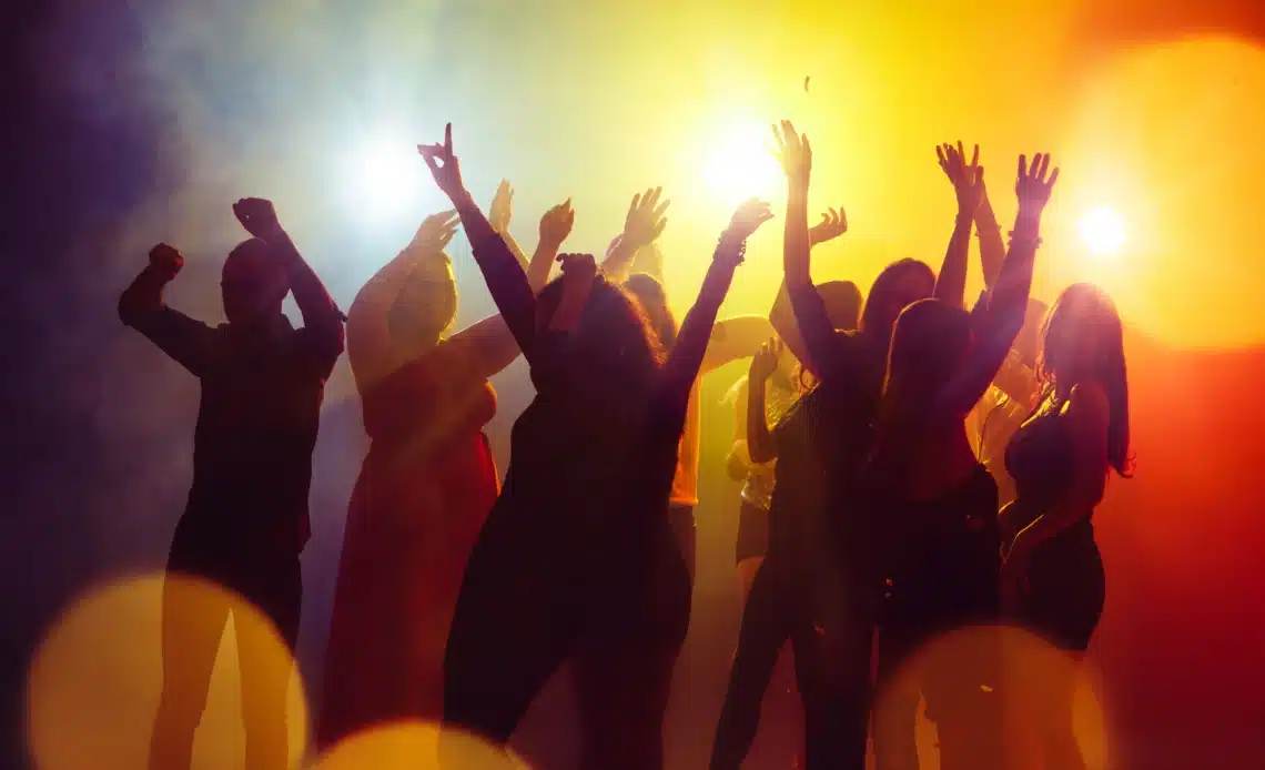 Un groupe de jeunes danse sous des lumières jaune et rouge, les mains en l'air, illustrant les situations pouvant conduire à des amendes pour tapage nocturne