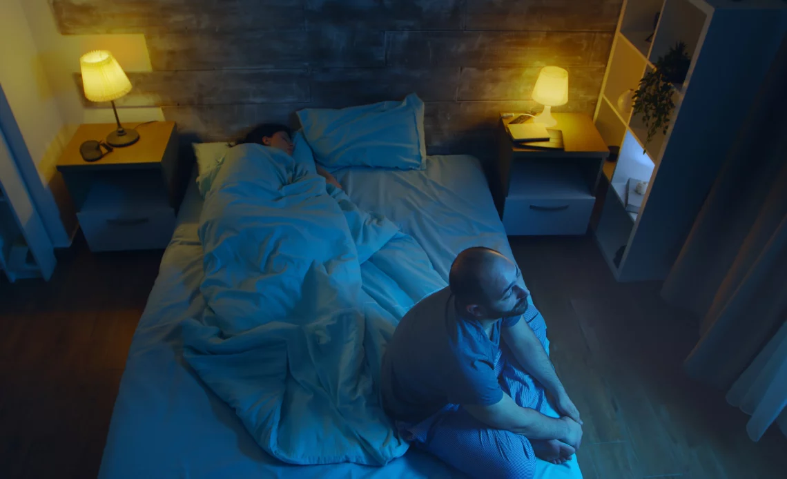 Un homme éveillé sur le bord du lit la nuit pour illustrer un tapage nocturne le week end