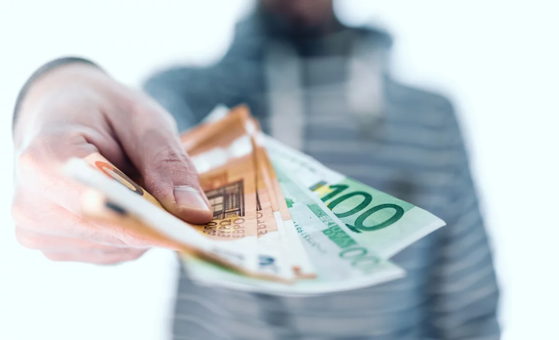 Un homme tend des billets pour illustrer combien on peut toucher en saisie sur salaire.