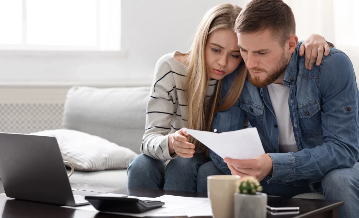 Un jeune couple assis sur un canapé tient un commandement de payer aux fins de saisie vente