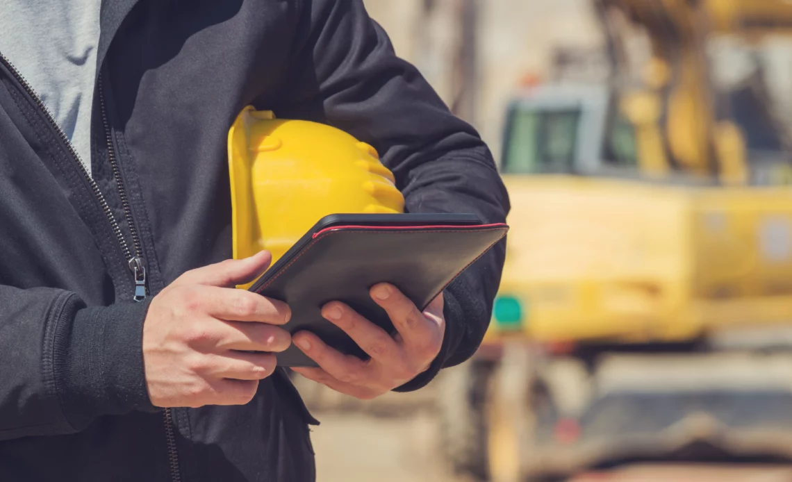 Un huissier avec un casque de chantier sous le bras et une tablette à la main fait un constat en matière de travaux